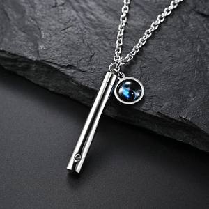 Détail d'un pendentif de parfum en acier avec breloque émaillée sur fond de pierre