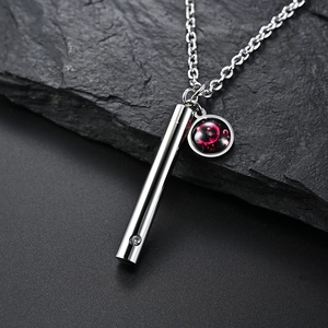 Détail macro du pendentif cylindre argenté et breloque nébuleuse sur pierre texturée sombre