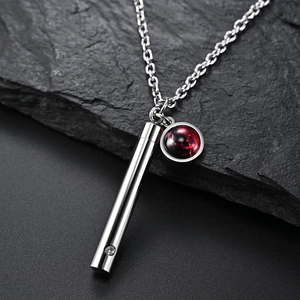Détail macro de pendentifs cylindre argent et pierre étoilée rouge sur chaîne fine