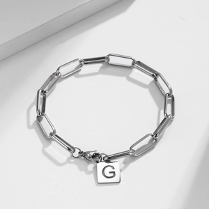 Detail of silver paperclip chain bracelet featuring a square cutout letter G pendant