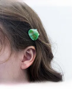 Detail of a green acetate cat hair claw clip worn on side wavy hair for styling