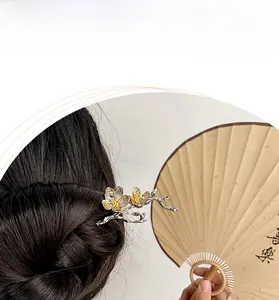 Detail of silver plum blossom hair pin with gold accents styled on dark hair with a fan