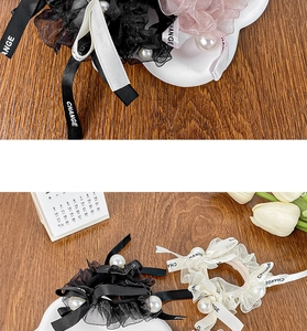 Detailed view of cream lace scrunchie with printed ribbon and large pearl accents