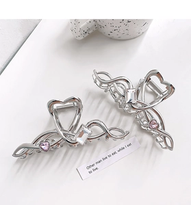 Detailed view of silver heart-shaped hair claw clips with pink zircon stones on white desk