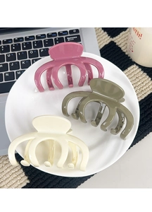 Close-up of three large glossy hair claws in pink, olive and cream on a ceramic tray