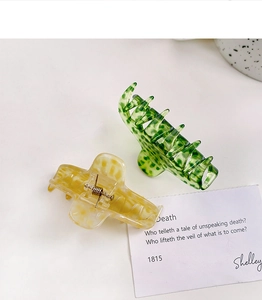 Detail view of two small leopard print acetate hair claws in dark green and amber tones