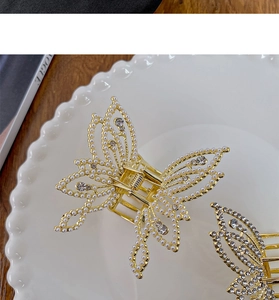 Detail of gold butterfly hair claw with pearls and rhinestones on a white plate