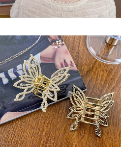 Close-up of golden butterfly hair claw clips with pearls and rhinestones on a wooden desk