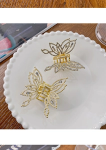 Detail of gold hollow butterfly hair claws with white pearls and rhinestones on a white plate
