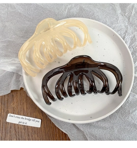 Top view of two large octopus hair claw clips in cream and brown on a ceramic plate