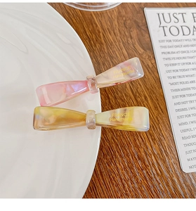 Detailed macro view of acetate bow hair clips featuring marbled resin and gold branding