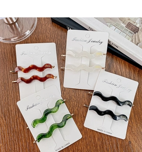 Close-up of wavy acetate hair clips in tortoise, cream, emerald, and black finishes