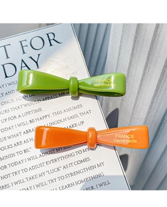 Detailed shot of handmade acetate bow hair clips in green and orange with gold lettering