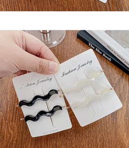 Detailed close-up of wave-shaped acetate hair clips in black and cream with gold label