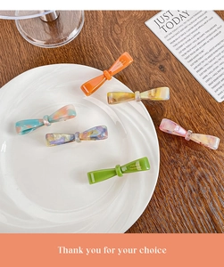 Flat lay of handmade acetate bow hair clips in assorted colors on a ceramic tray