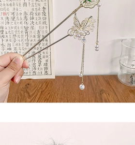Détail d'une épingle à cheveux papillon dorée avec perles blanches et longs glands