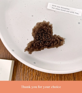 Détail d'une pince à cheveux en peluche marron avec texture laine d'agneau sur assiette blanche