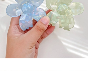 Close-up of floral hair claw clips with iridescent pearlescent finish in blue and green