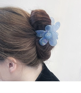 Detailed back view of a blue iridescent flower hair claw clip on dark hair