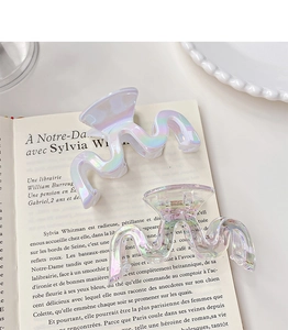 Macro view of wave-shaped iridescent hair claws on French book pages with rainbow reflections