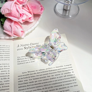 Iridescent butterfly hair claw clip with colorful pearlescent finish on a book