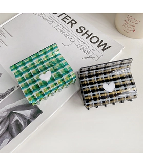 Detail of green and black plaid claw clips featuring a white heart charm and tweed texture