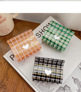 Close-up of three checkered hair claws with heart accents on a white magazine and table
