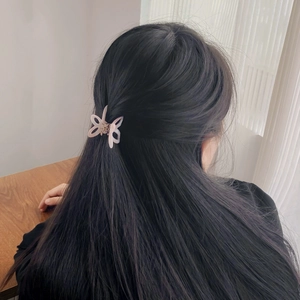 Pince à cheveux papillon évidée avec finition rose irisée sur de longs cheveux sombres