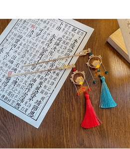 Detail of Chinese lotus hairpins with long tassels in red and blue on a wooden desk