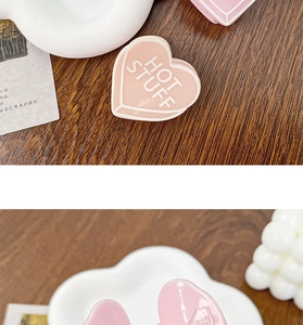 Détail d'une pince à cheveux en acrylique rose pêche en forme de cœur avec lettrage