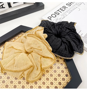 Close-up of black and beige fabric hair scrunchies with elegant gold metallic stitched edges