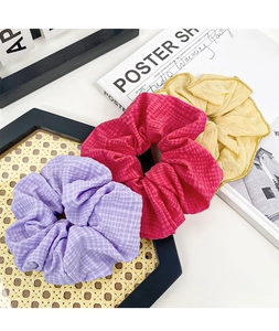 Detail of luxury fabric scrunchies in purple and yellow on a textured black tray