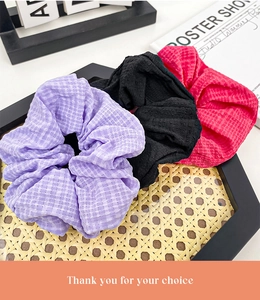 Close-up of three textured fabric scrunchies in purple, black, and rose on a rattan tray