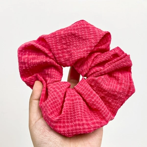Elegant red oversized scrunchie with metallic grid texture held against white background