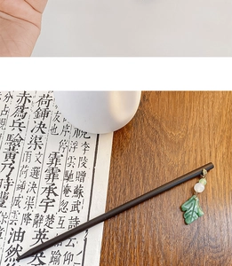 Detail view of a vintage dark wood hair stick with a white bead and green leaf pendant