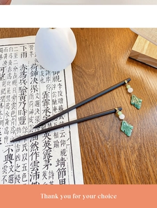 Close-up of wooden hair sticks with green jade-like beads and gold leaf charms