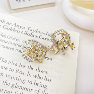Mini goldene Blumen-Haarklammern mit rosa Emaille und Kristallen auf einer Buchseite