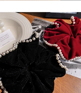 Detail of velvet pearl hair ties in burgundy and black on a textured wooden table