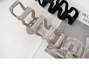Detail of matte wave-shaped hair claws in khaki and black over a fashion magazine