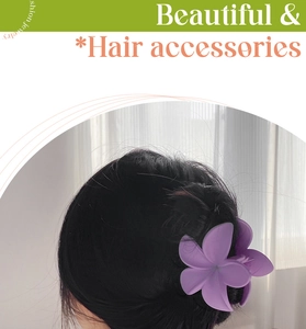 Detail view of a matte purple plumeria hair claw clip worn on a neat black hair bun