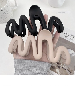 Detail showing oversized wave-design hair claws in matte black and beige resin colors