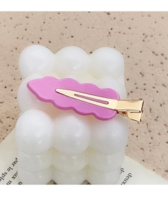 Close-up of pink wavy acrylic hair clip with gold metal clip on white bubble texture