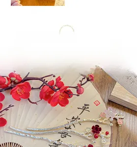 Close-up of golden plum blossom hairpin with red petals and pearl tassels on a fan