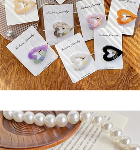 Detail of vintage heart-shaped acetate hair clip with marble pattern and pearl necklace