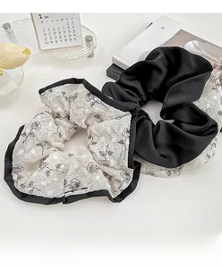 Detail view of lace rose embroidery scrunchie and black satin hair tie on artistic background