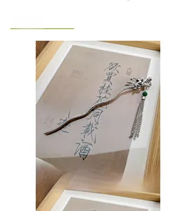 Detailed silver dragon hair pin with green bead and metal tassels on calligraphy