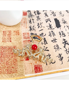 Detailed close-up of golden dragon hair claw clip with large red pearl on calligraphy paper