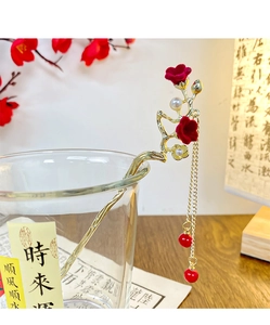 Detailed view of red floral hair stick with golden tassels and pearls on a wooden desk