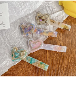 Detail of four acetate heart hair clips in marble texture with rhinestones and gold lettering