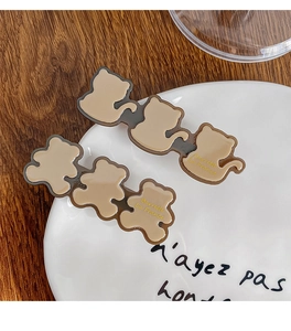 Close-up of French acetate cat and bear hair clips on a vintage wooden desk surface
